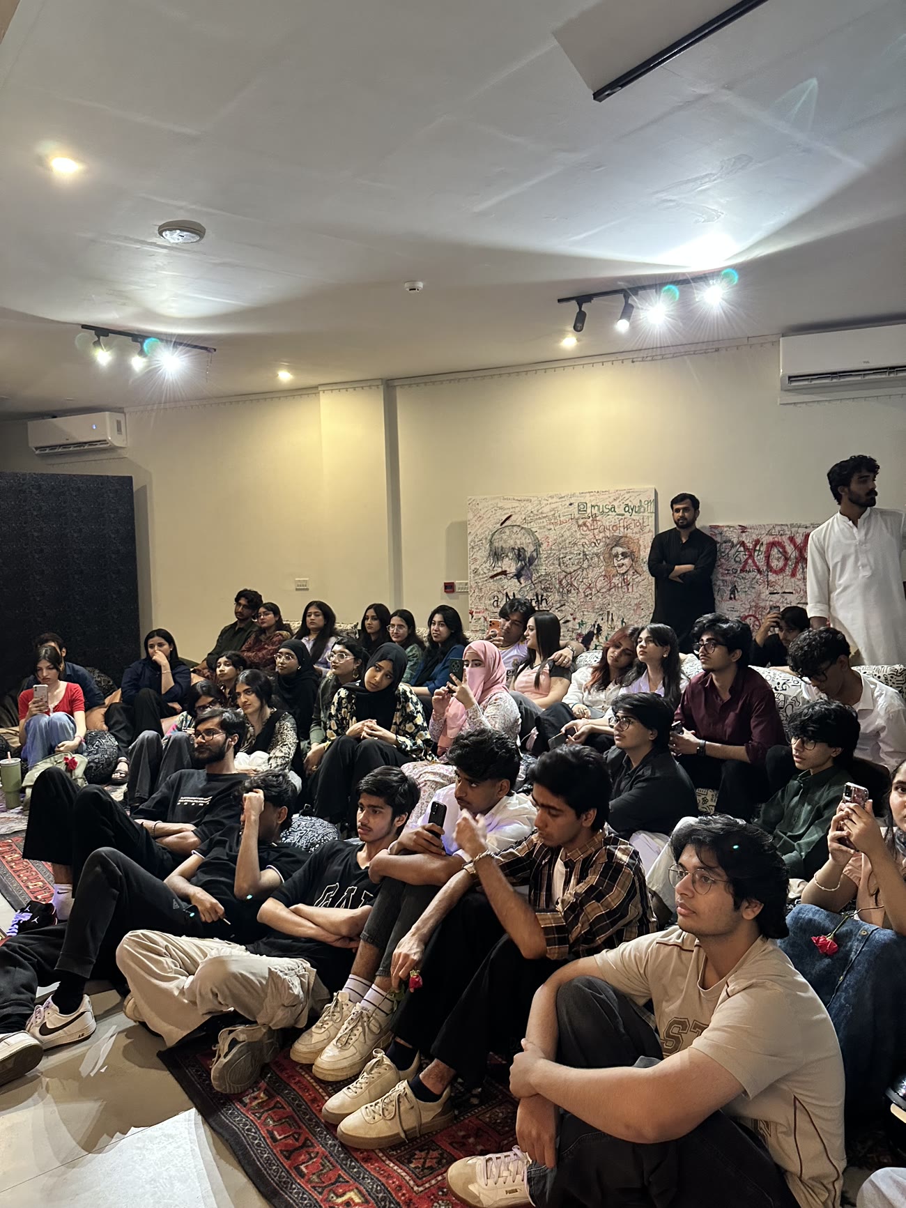 A packed room of listeners seated on rugs