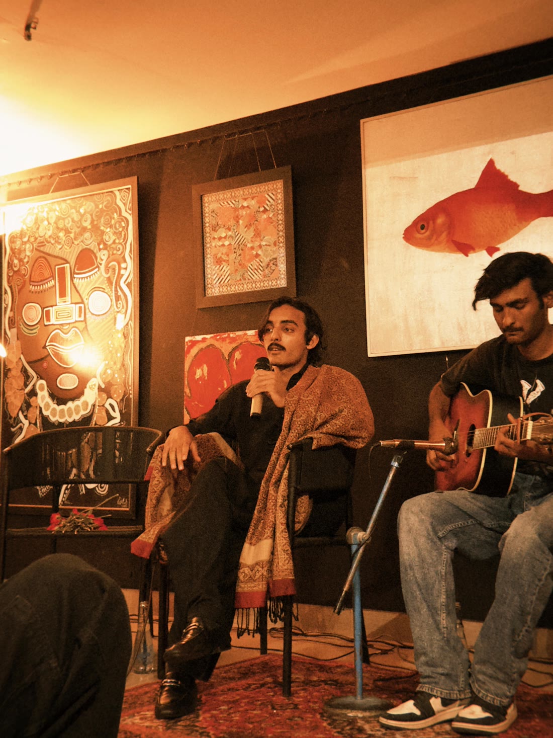 Mirza seated with a guitarist among hanging artwork